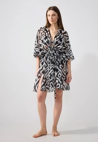 Genomskinlig svartvit kaftan med ett djärvt djurtryck, djup V-ringning, markerad midja och korta ärmar med slits upp till låret.