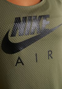 Top deportivo de color verde oliva con superficie texturizada, que presenta un destacado logo de Nike en negro y la palabra "AIR" impresa en letras negritas.