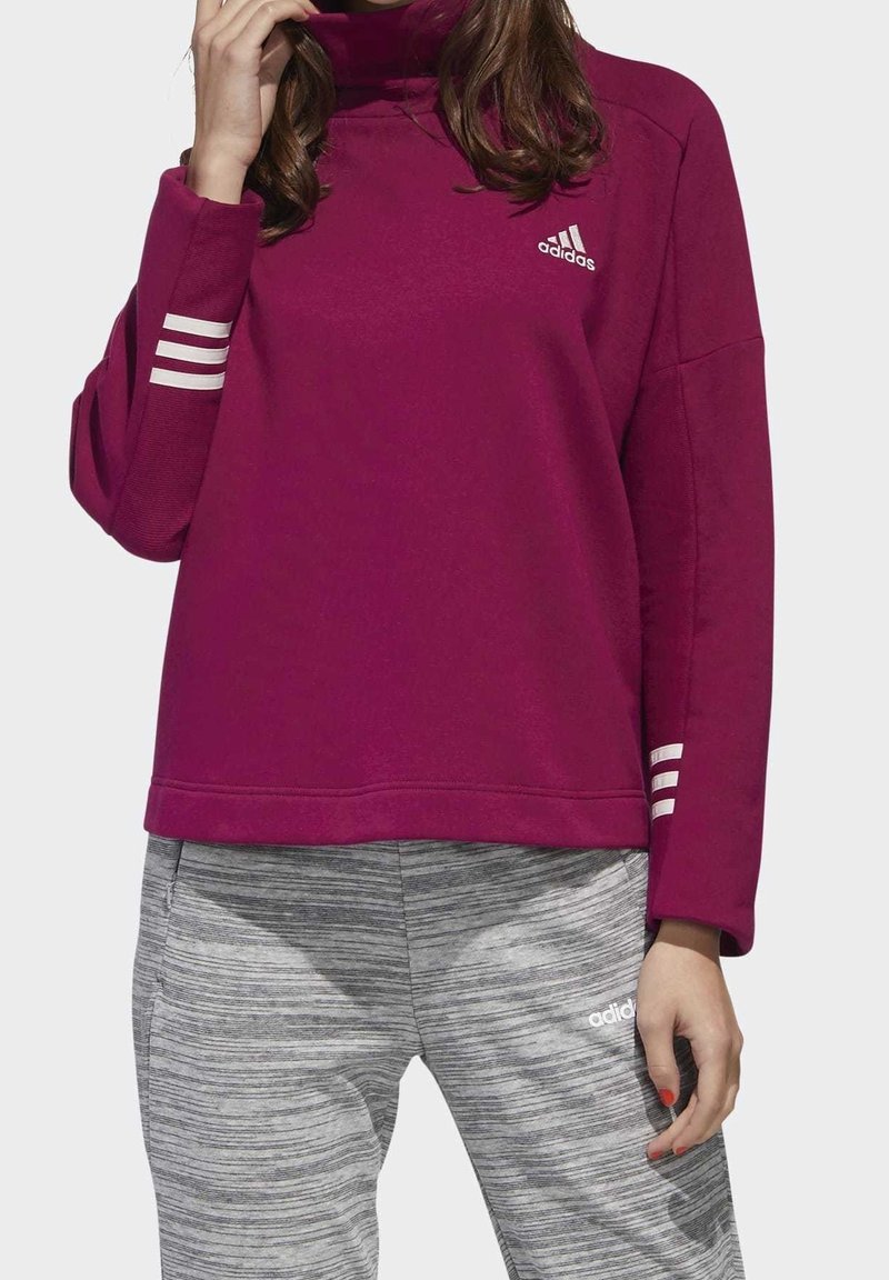 Person som bär en burgunderfärgad Adidas-tröja med vita ränder på ärmarna och grå Adidas-träningsbyxor med randigt mönster.