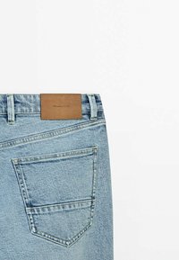 Vue arrière d'un jean en denim bleu clair avec une seule poche et une étiquette de marque en cuir marron sur la ceinture.