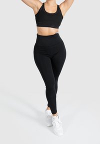 Mustat urheilulliset cropped-top ja korkeavyötäröiset legginsit, joissa on sileä pinta ja joustava kangas. Yhdistetty valkoisiin urheilujalkineisiin.