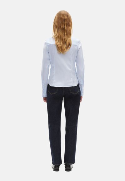 Camisa de manga larga azul claro con una textura elegante y suave, combinada con jeans oscuros de pierna recta. Ajuste slim, diseño simple, costuras suaves.
