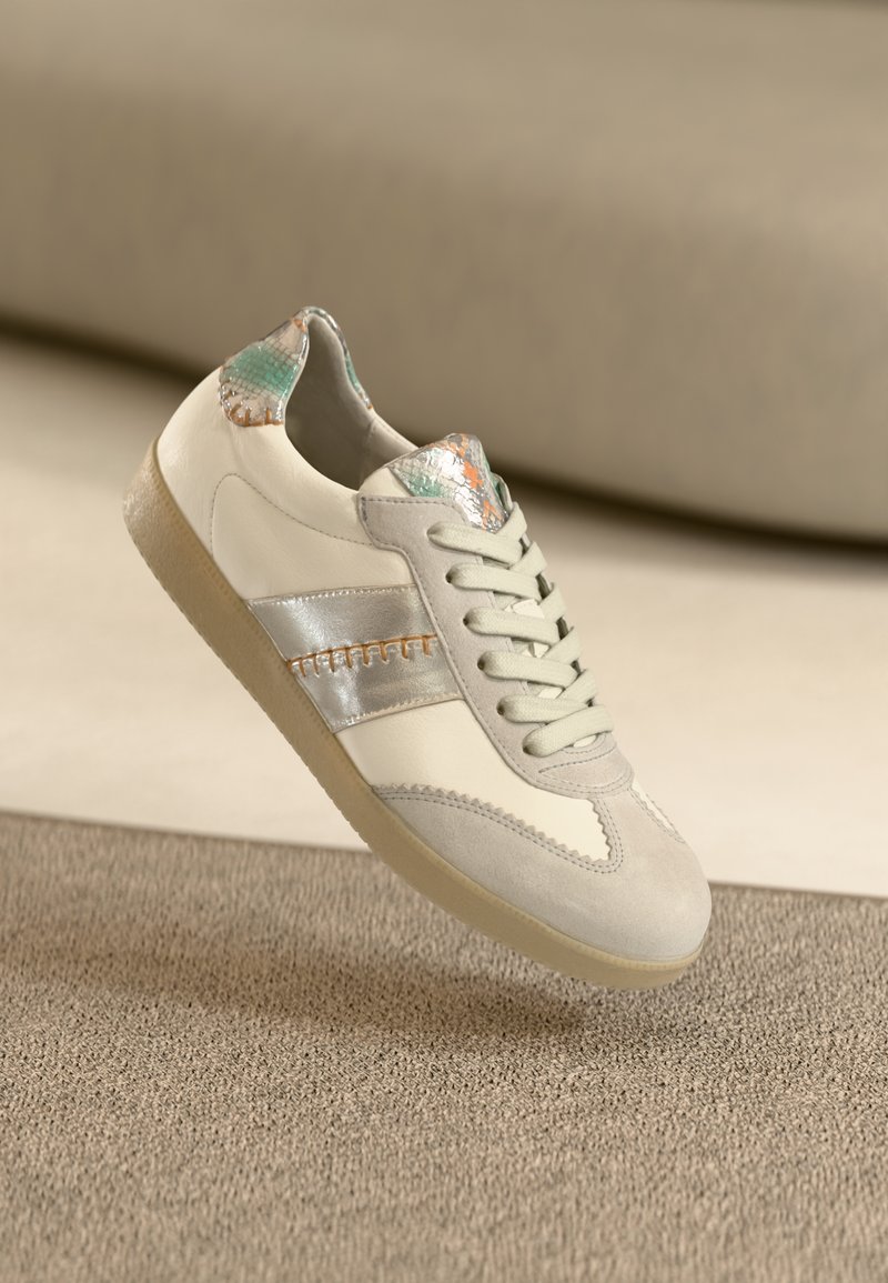 Hellbeiger Sneaker mit silbernen Akzenten, strukturierter Zunge in Grün und Orange, glattem Leder und weichem Wildleder, mit einer Gummisohle.