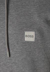 Grijze hoodie met een zachte textuur, voorzien van een rechthoekige BOSS-logo patch in lichtgrijs, en een trekkoord met een grijze stopper.
