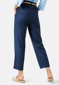 Námořnické modré lněné kalhoty s rovnými nohavicemi, se širším pasem, bočními kapsami a zadní kapsou, obuté s béžovými nazouvacími botami.