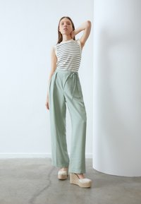 Hvidstribet ærmeløs top iført med højtaljede mintgrønne vide bukser og beige espadrille platform sko. Glatte teksturer, elegant fald.
