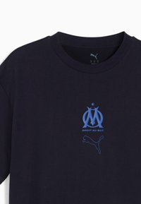 Jūras zila kokvilnas T-krekls ar zilu grafiku, kurā redzams Olimpiķu de Marseļas logo un teksts "DROIT AU BUT" zem Puma logo.