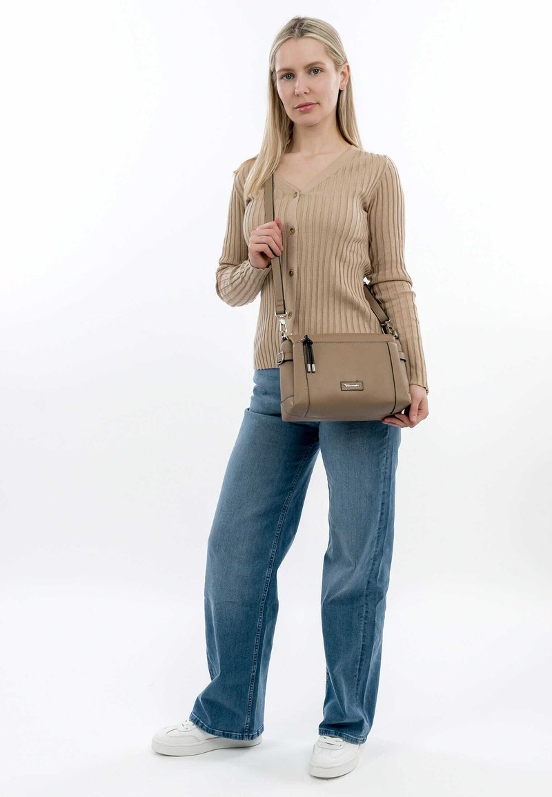 Beige handbag with a smooth texture, zip closures, and a removable strap, carried with a beige ribbed top and blue jeans.