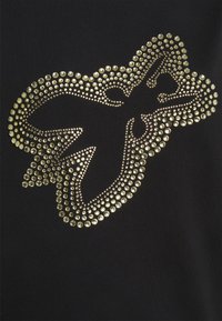 Camiseta de tela negra con un gran patrón decorativo dorado hecho de tachuelas de diferentes tamaños en forma de mariposa.