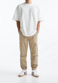 Hvid oversized t-shirt, beige cargo bukser med side lommer, elastiske manchetter, og hvide sneakers med sorte detaljer.