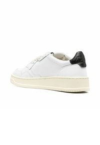 Sneaker bianca in pelle con un accento nero sul tallone, superficie testurizzata, suola beige e lacci grigio chiaro. Design classico low-top.