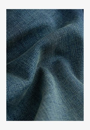 Tissu en denim bleu foncé avec un tissage texturé, montrant de profondes variations de couleur indigo et une apparence douce et froissée.