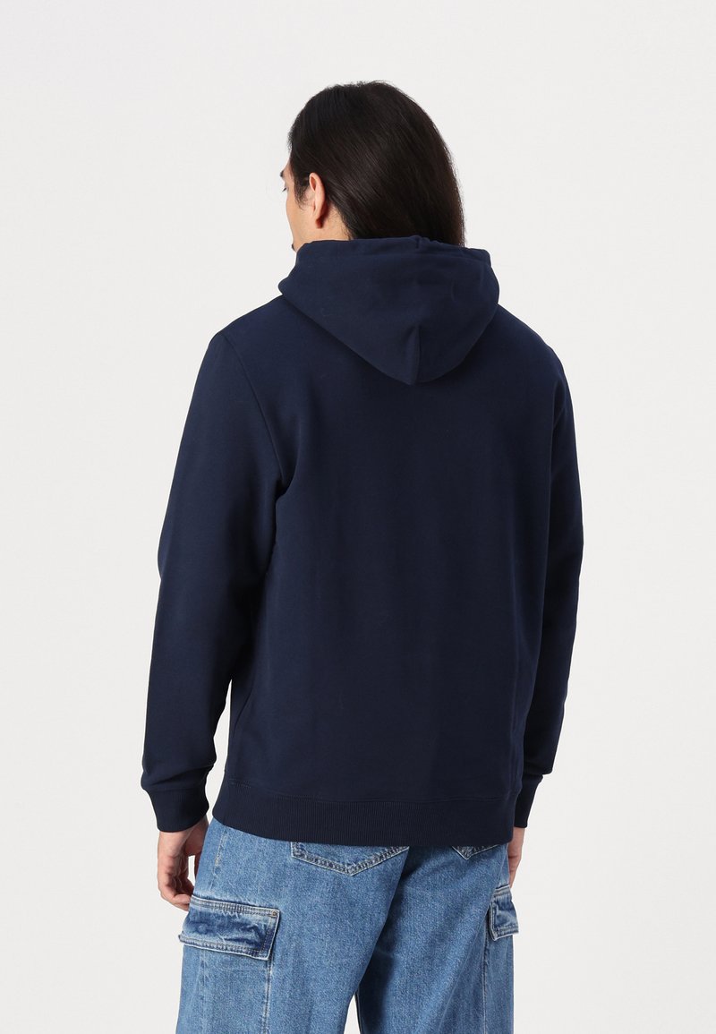Felpa blu navy con cappuccio regolabile e polsini a costine, abbinata a pantaloni cargo blu chiaro con multiple tasche.
