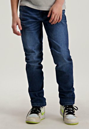 Donkerblauwe denim jeans met een rechte snit, voorzien van subtiele stiksels, gecombineerd met witte sneakers met groene accenten.