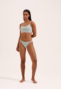 Bralette verde claro com banda de logótipo branca, cuecas de biquíni combinando. Design simples, forma ajustada, tecido macio, costuras mínimas.