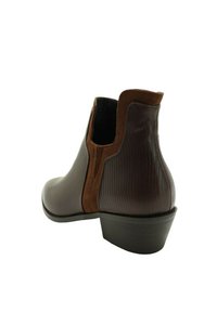 Botín marrón hasta el tobillo con cuero texturizado, borde de ante, paneles laterales elásticos y tacón bajo apilado, angularmente posicionado para mostrar la parte posterior y lateral.