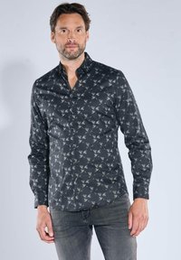 Langärmeliges schwarzes Hemd mit einem dezenten Vogelmuster, Knopfleiste vorn und Kragen. Der Stoff ist glatt mit leichtem Glanz. Kombiniert mit grauen Jeans.