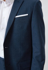 Marineblauwe geblokte blazer met notch-lapels, enkele borstzak met witte accent, zachte textuur, getailleerde pasvorm en soepele knoopsluitingen.