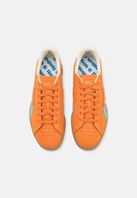 Oranžové semišové tenisky se světle modrými akcenty a perforovanou špičkou. Bílé polstrované límce a modrý vzorovaný stélka s logem "Reebok".