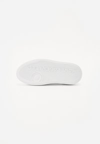 Suola di sneaker bianca con un motivo testurizzato, caratterizzato da scanalature e un dettaglio di logo rotondo. La superficie è liscia e piatta, progettata per il comfort.