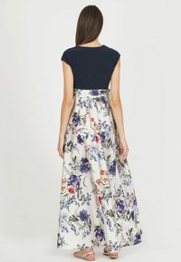 Robe maxi avec un haut bleu marine et une jupe à motif floral, ornée de fleurs multicolores sur fond blanc. Tissu doux et design fluide.