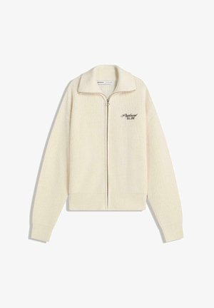Crèmekleurige gebreide zip-up trui met een kraag en zwarte geborduurde tekst op de borst met de tekst "Professional Est. 2001."