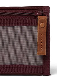 Pochette en tissu bordeaux avec un panneau en maille, dotée d'une fermeture éclair et d'un accent en cuir marron avec un bouton pression. Texture lisse dans l'ensemble.