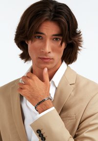 Črn in srebrn zapestnica na zapestju, ki se ponaša z geometrijskim dizajnom in gladko površino, postavljena ob svetlo obleko in belo srajco.