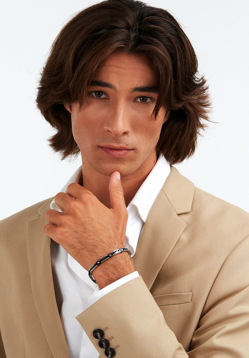 Črn in srebrn zapestnica na zapestju, ki se ponaša z geometrijskim dizajnom in gladko površino, postavljena ob svetlo obleko in belo srajco.