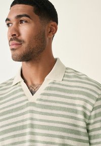 Polo en rayas verde claro y crema, con un patrón de punto texturizado y un cuello blanco acanalado con un diseño de escote en V.