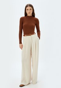 Maglia lunga a maniche con righe marrone, con scollo scallop, abbinata a pantaloni larghi crema e una cintura color nocciola, completata da scarpe basse marroni.
