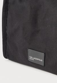 Čierna textilná taška s textúrovaným povrchom, obdĺžnikového tvaru a výraznou nálepkou s nápisom "KARL LAGERFELD JEANS."
