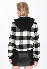 Hoodie a scacchi bianco e nero con cappuccio nero, design cropped e tessuto texturizzato, abbinato a una mini gonna in pelle nera.