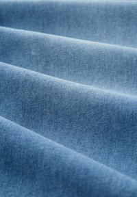 Denim audums gaiši zila krāsā, ar gludu tekstūru un salocītām kārtām, kas izceļ tā mīkstumu un vieglu spīdumu.