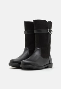 Paire de bottes mi-mollet noires avec l'avant en cuir lisse, le dessus en suède, et une sangle décorative ornée d'une boucle en forme de cœur argentée.
