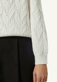 White knitted sweater featuring a diamond pattern, ribbed cuffs, and soft texture, paired with black fabric pants.