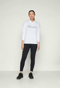 Felpa bianca con logo "Champion", abbinata a leggings neri e sneakers nere. Tessuto morbido con una vestibilità rilassata, dotata di una tasca frontale.