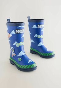Modré gumové boty na dešť s motivem Sonica the Hedgehog, zdobené vzory oblaků a prstenů, zeleným chevronovým lemem a nálepkami s postavami na bílém pozadí.