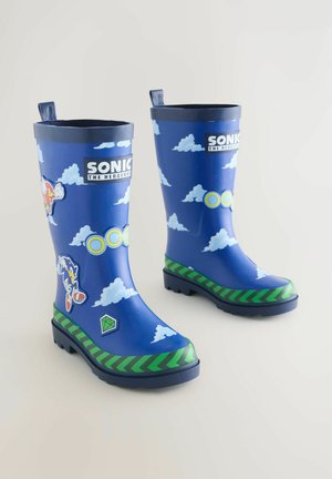 Blauwe Sonic the Hedgehog-regenlaarzen met patronen van wolken en ringen, groene chevronrand en karakterstickers op een witte achtergrond.
