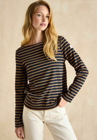 Langärmliges, navy- und senfgelb gestreiftes Shirt mit Rundhalsausschnitt, aus weichem Stoff, in lockerer Passform, kombiniert mit cremefarbener Hose.