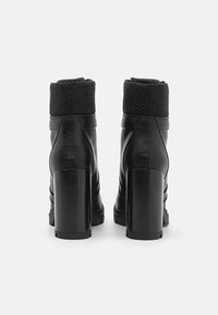 Bottes à cheville en cuir noir avec un col en maille noire texturée et des talons blocs épais et brillants. Caractérisées par un détail de couture verticale.