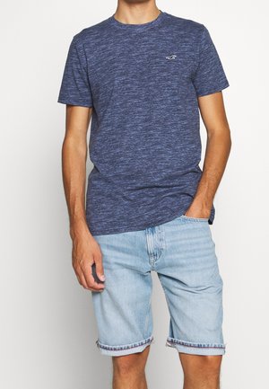 Granatowy t-shirt z krótkim rękawem wykonany z fakturowanej tkaniny, zestawiony z jasnoniebieskimi szortami dżinsowymi z podwiniętymi mankietami i kontrastowym obszyciem.