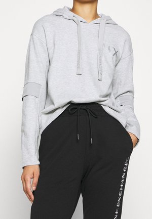 Sweat à capuche gris avec manches longues, poche avant et cordon de serrage. Associé à un pantalon noir arborant un logo vertical blanc sur une jambe.