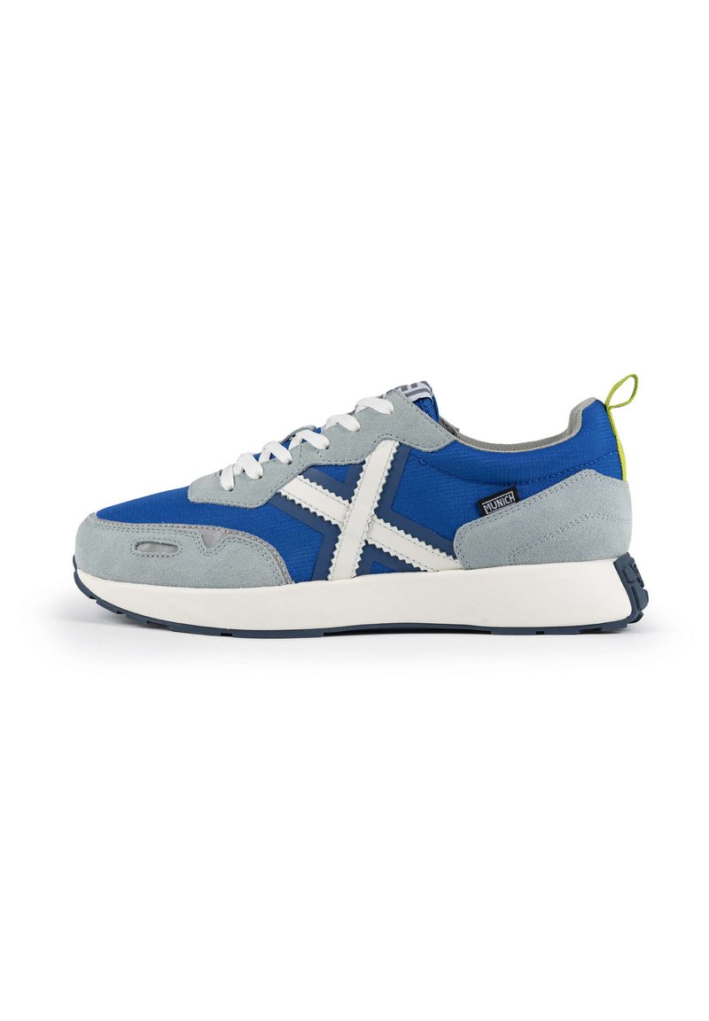 Zapatillas azules y grises con parte superior de tela y gamuza, acentos blancos, puntera redondeada y suela texturizada. Incluye un tirador amarillo en el talón.