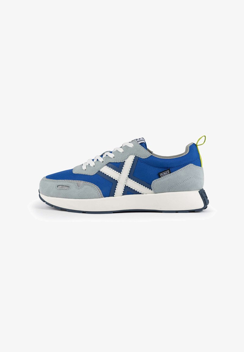 Zapatillas azules y grises con parte superior de tela y gamuza, acentos blancos, puntera redondeada y suela texturizada. Incluye un tirador amarillo en el talón.