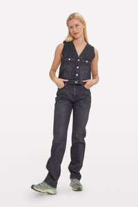 Schwarzes Jeansweste-Oberteil mit V-Ausschnitt und Knöpfen, kombiniert mit passenden schwarzen geraden Jeans und grünen Sportschuhen.