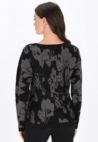Maglione nero con un motivo floreale argentato, con polsini e orlo a coste, dalla vestibilità rilassata e una consistenza morbida, visto da dietro.