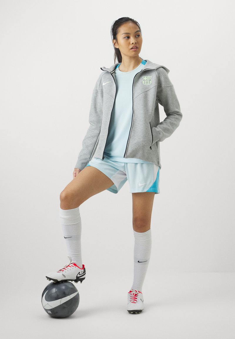 Casualny strój sportowy Nike składający się z szarego kaptura na zamek, jasnoniebieskiej koszulki oraz szortów w odcieniu aqua. Białe skarpetki i korki z czerwonymi akcentami.