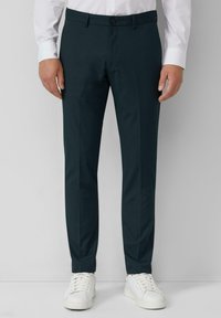 Pantalons taillés vert foncé avec une texture lisse, comprenant une fermeture à bouton à l'avant et des poches latérales, associés à des baskets blanches.