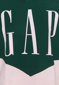 Tissu vert et rose pâle avec de grandes lettres blanches formant le mot "GAP" au centre.